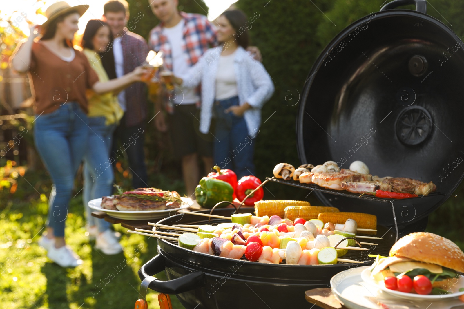 Photo of Group of friends having party outdoors. Focus on barbecue grill with food