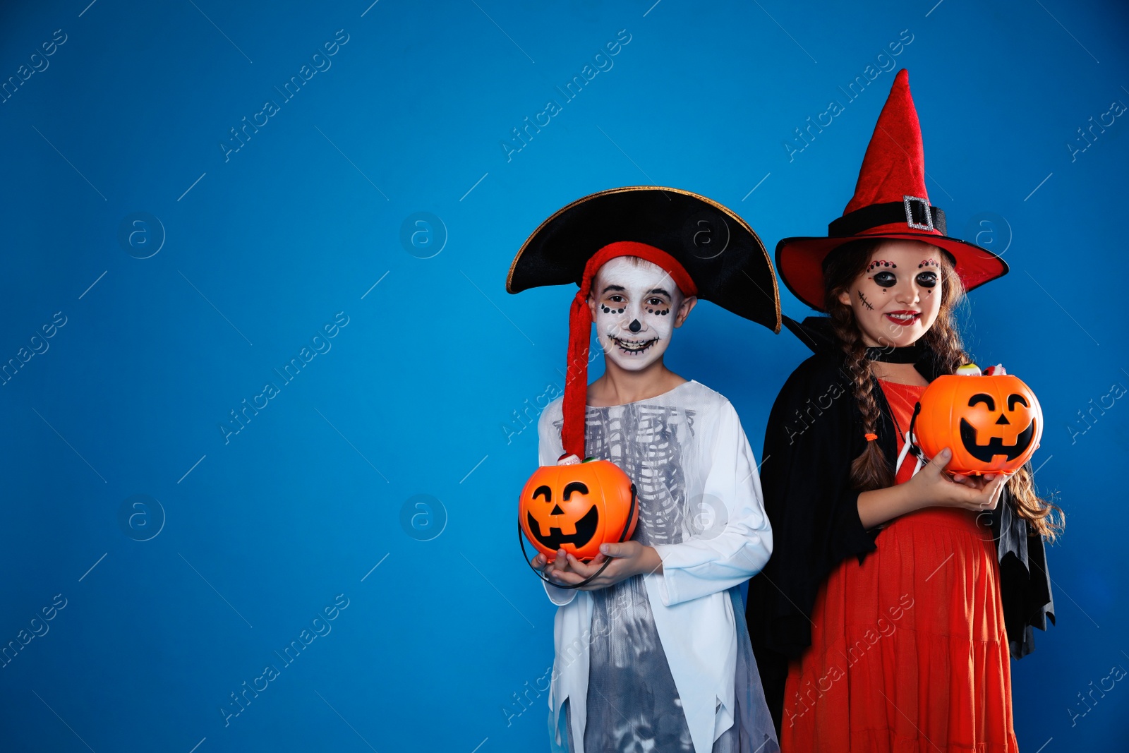 Photo of Cute little kids with pumpkin candy buckets wearing Halloween costumes on blue background. Space for text
