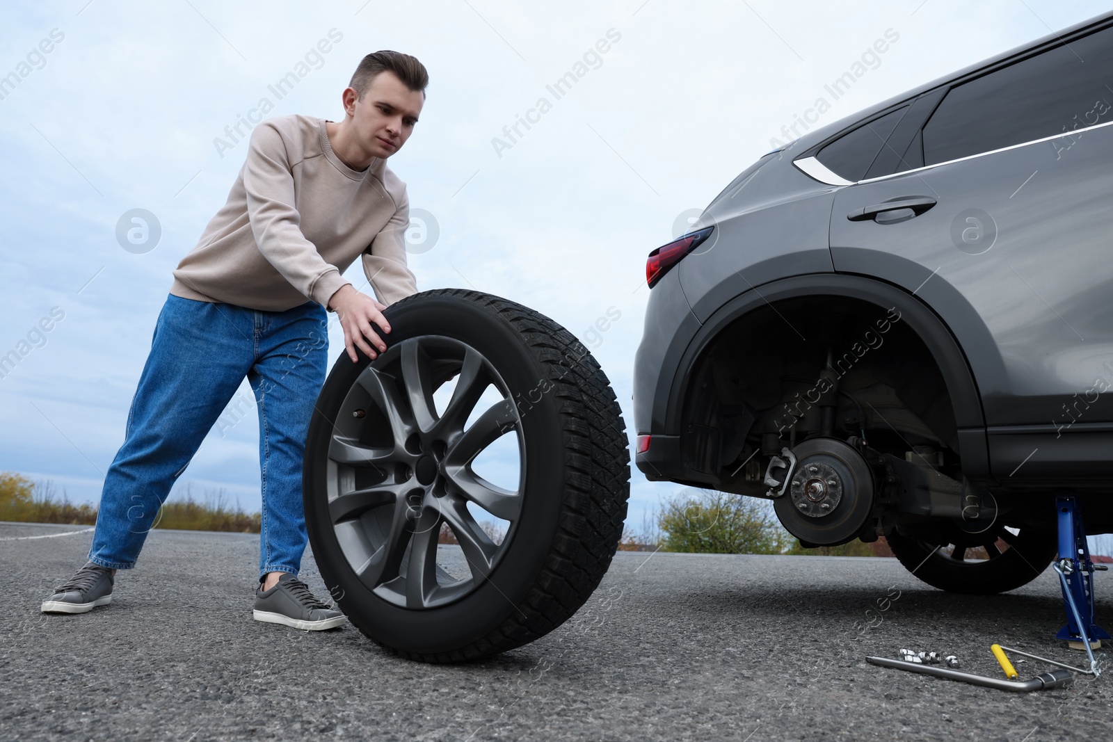 Photo of Young man changing tire of car on roadside