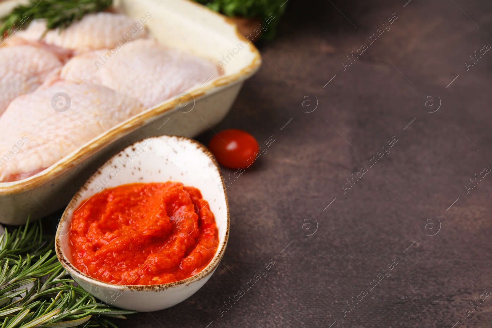 Photo of Fresh marinade, raw chicken and rosemary on brown table, closeup. Space for text