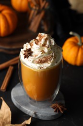 Photo of Glass of pumpkin spice latte with whipped cream and ingredients on black table