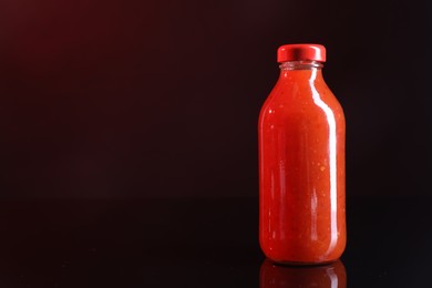 Photo of Spicy chili sauce in bottle against dark background, space for text