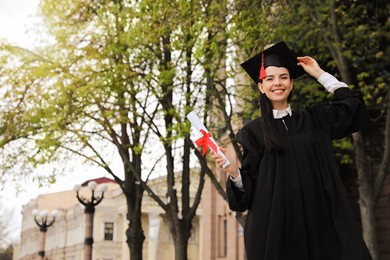 Happy student with diploma after graduation ceremony outdoors. Space for text