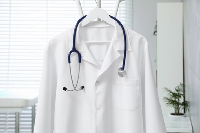 Photo of White doctor's gown and stethoscope hanging on rack in clinic, closeup
