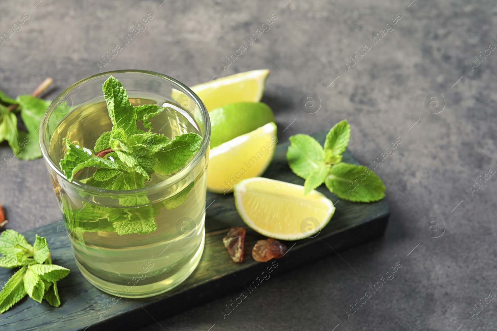 Photo of Glass with hot aromatic mint tea, fresh leaves and lime on table