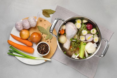 Photo of Pot and different ingredients for cooking tasty bouillon on light grey table, flat lay