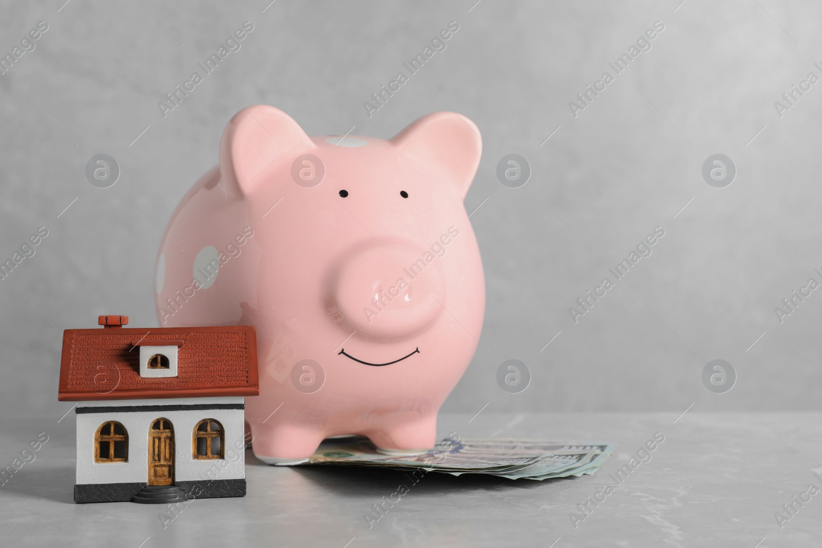 Photo of Piggy bank, dollar banknotes and house model on grey marble table. Space for text