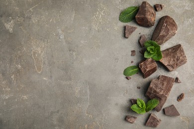 Tasty dark chocolate pieces with mint on grey table, flat lay. Space for text