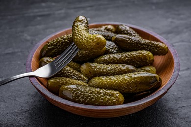 Photo of Wooden bowl of pickled cucumbers with fork on black table, closeup