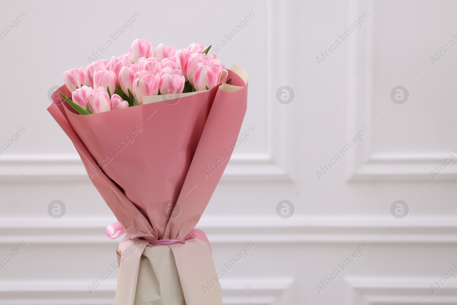 Photo of Beautiful bouquet of fresh pink tulips near white wall. Space for text