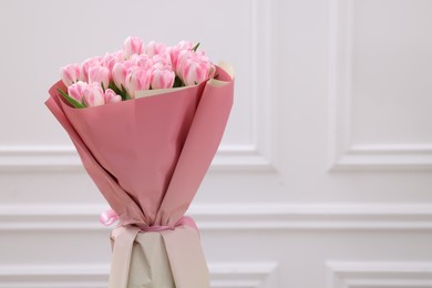 Photo of Beautiful bouquet of fresh pink tulips near white wall. Space for text