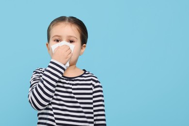 Photo of Girl blowing nose in tissue on light blue background, space for text. Cold symptoms