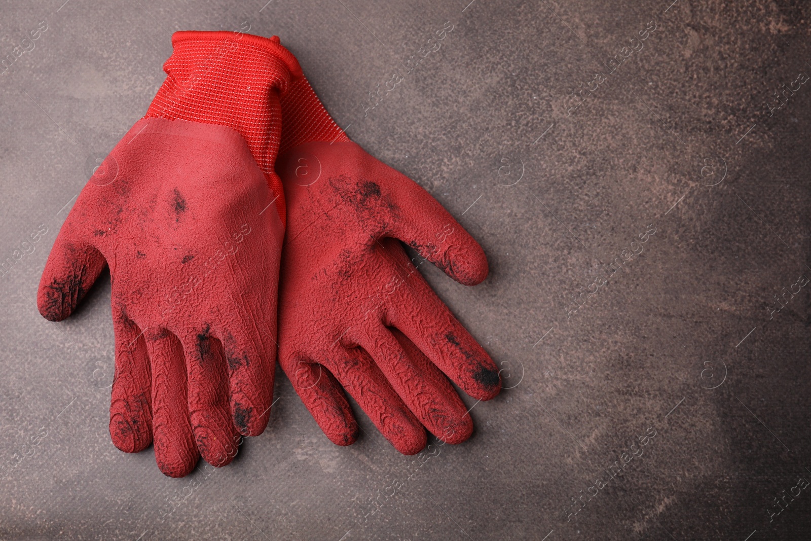 Photo of Pair of red gardening gloves on brown textured table, top view. Space for text