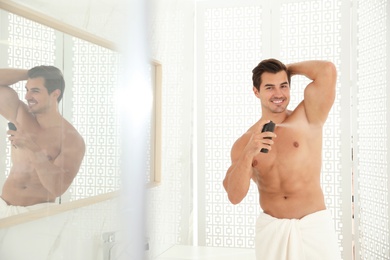 Handsome young man applying deodorant in bathroom