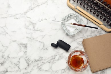 Photo of Glass ashtray with long cigarettes holder, lighter and alcohol drink near vintage typewriter on white marble table, flat lay. Space for text