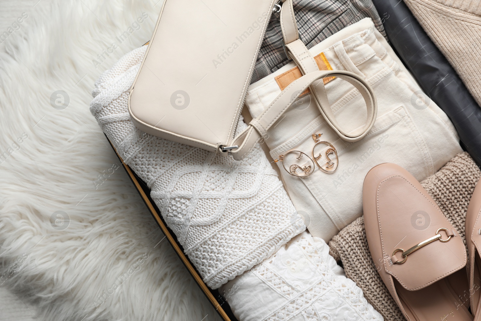 Photo of Open suitcase with folded clothes, shoes and accessories on rug, top view