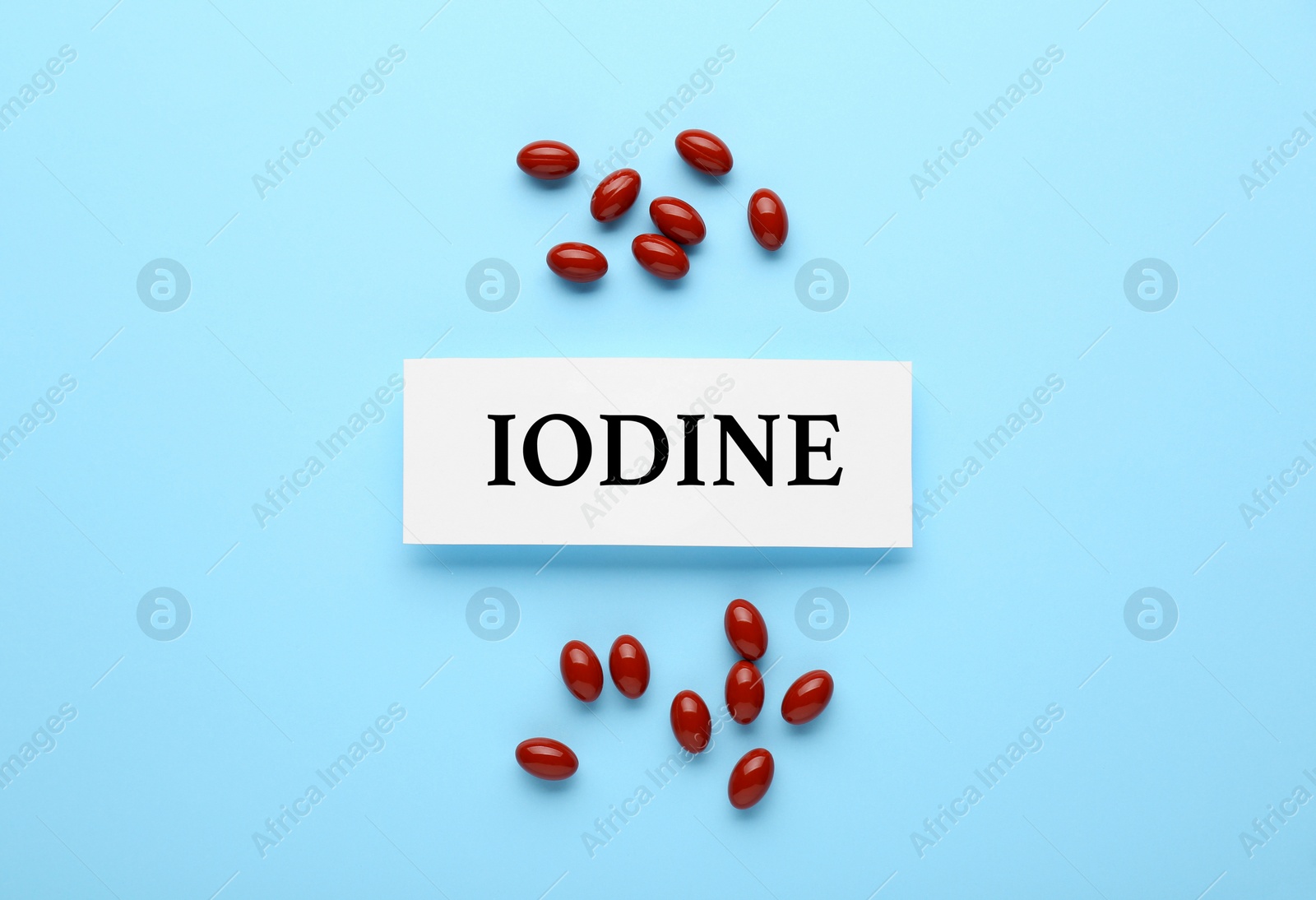 Photo of Card with word Iodine and pills on light blue background, flat lay