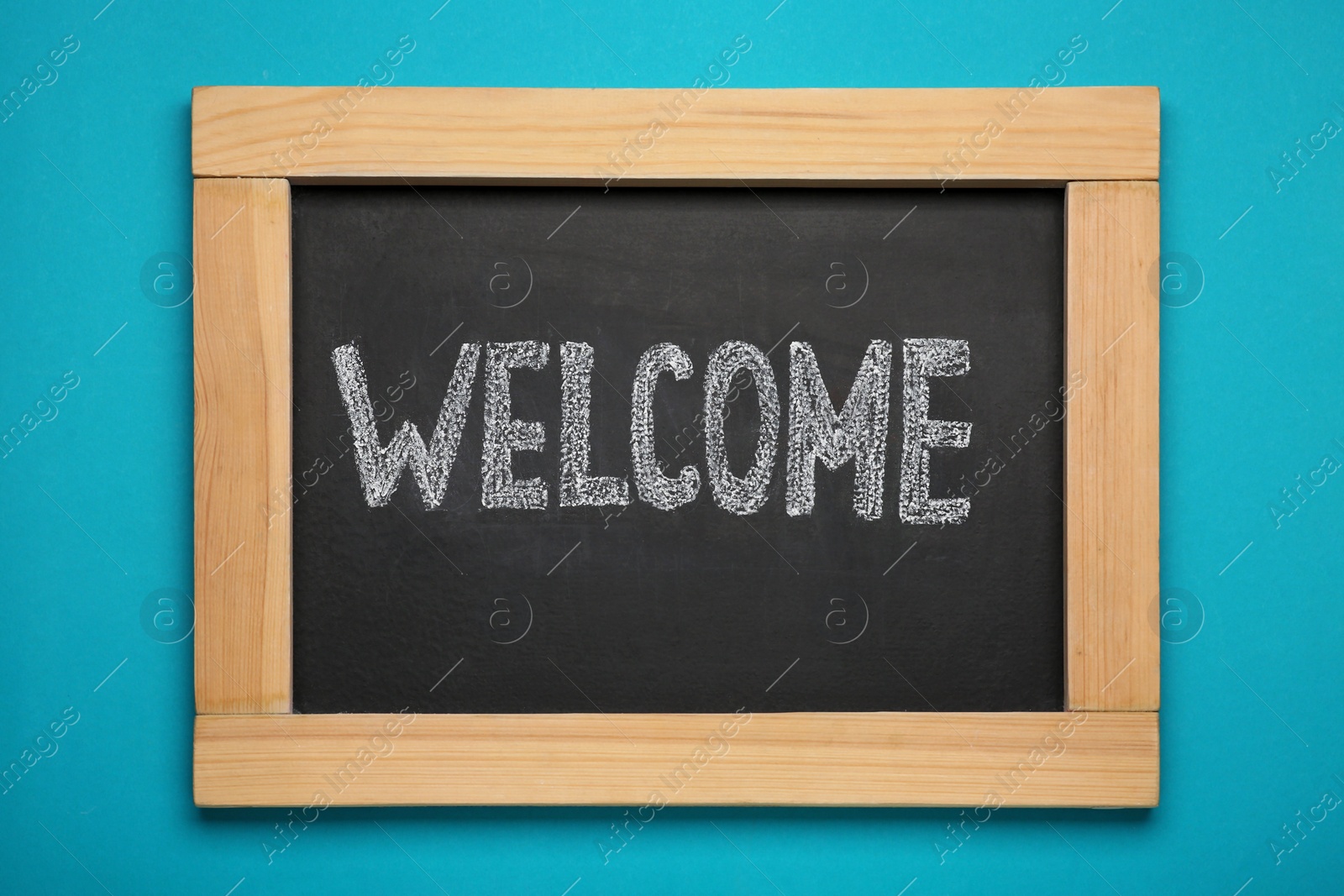 Photo of Small chalkboard with word Welcome on turquoise background, top view