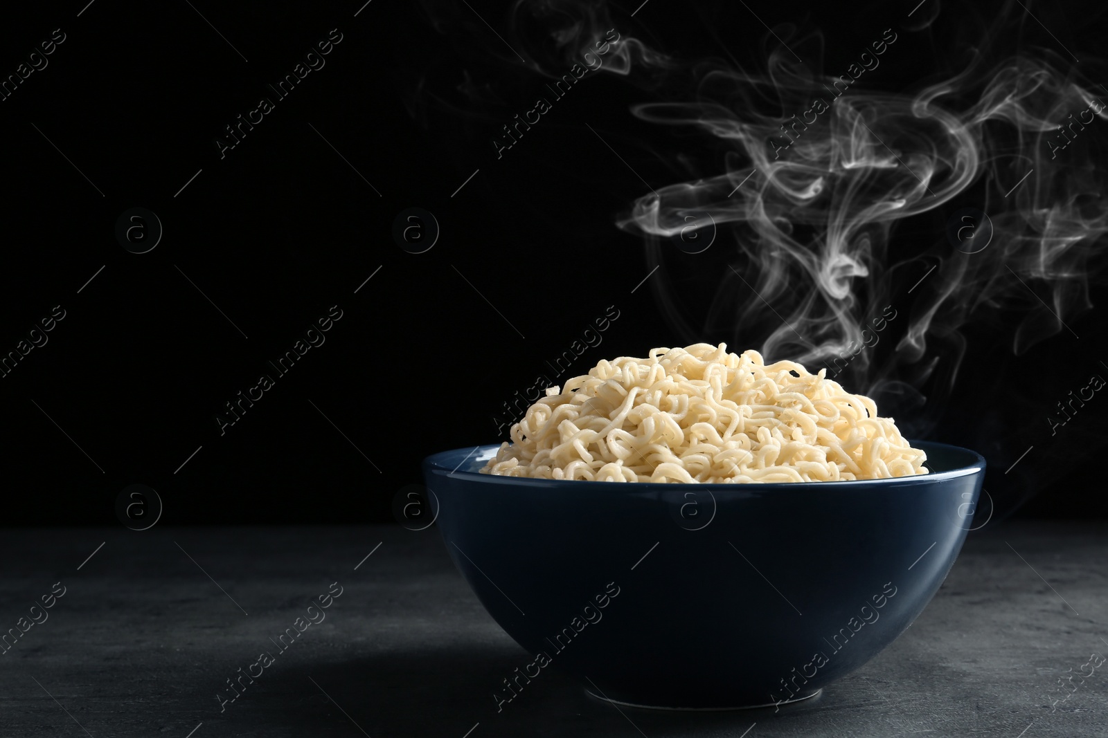 Photo of Bowl of hot noodles on table against black background. Space for text