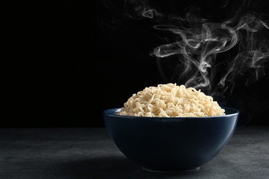 Photo of Bowl of hot noodles on table against black background. Space for text