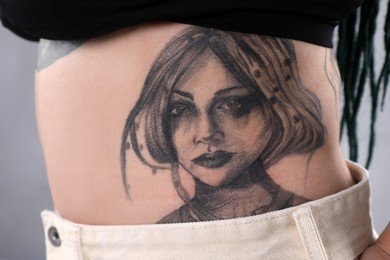 Photo of Woman with tattoos on body against grey background, closeup
