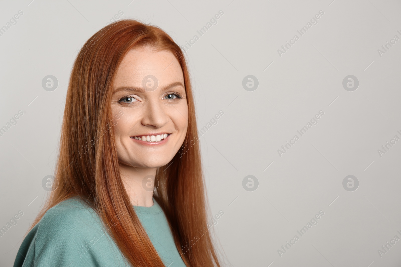 Photo of Candid portrait of happy young woman with charming smile and gorgeous red hair on light background, space for text