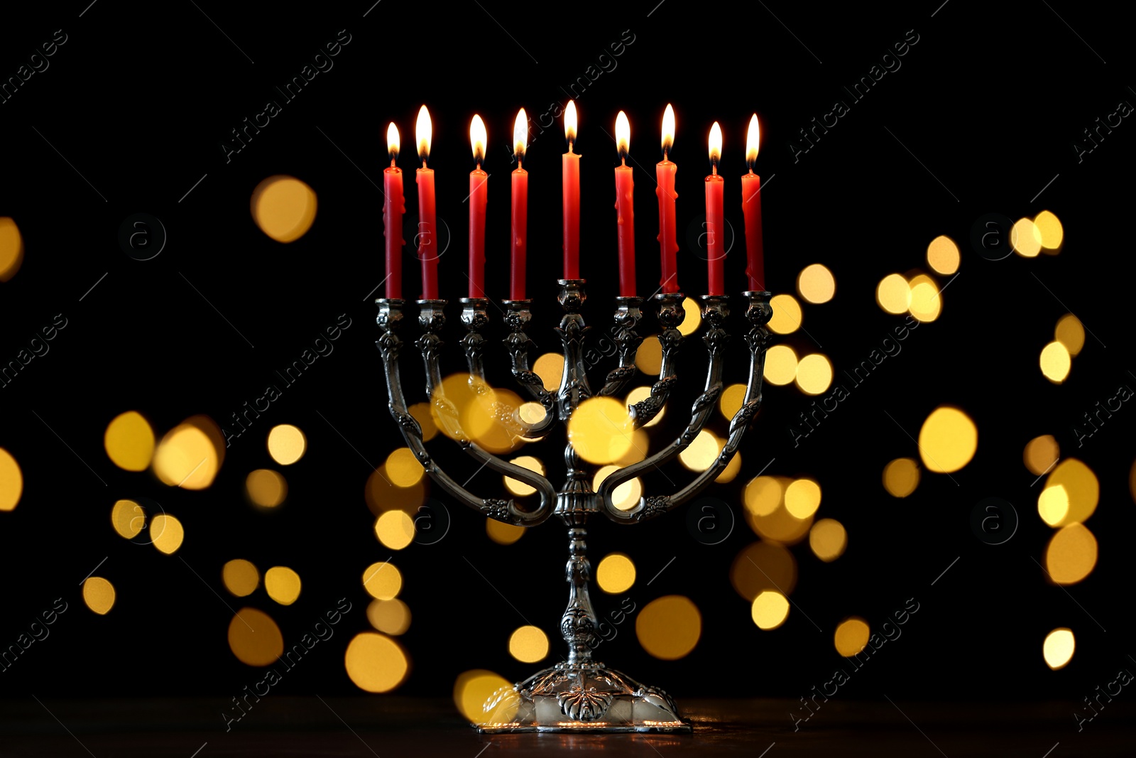 Photo of Silver menorah with burning candles against dark background and blurred festive lights. Hanukkah celebration