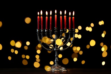 Silver menorah with burning candles against dark background and blurred festive lights. Hanukkah celebration