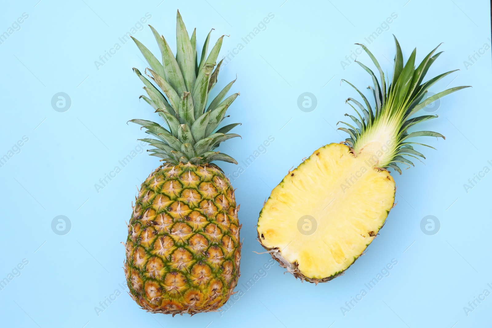 Photo of Whole and cut ripe pineapples on light blue background, flat lay