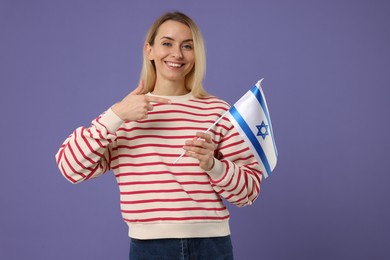 Photo of Happy woman pointing at flag of Israel on violet background