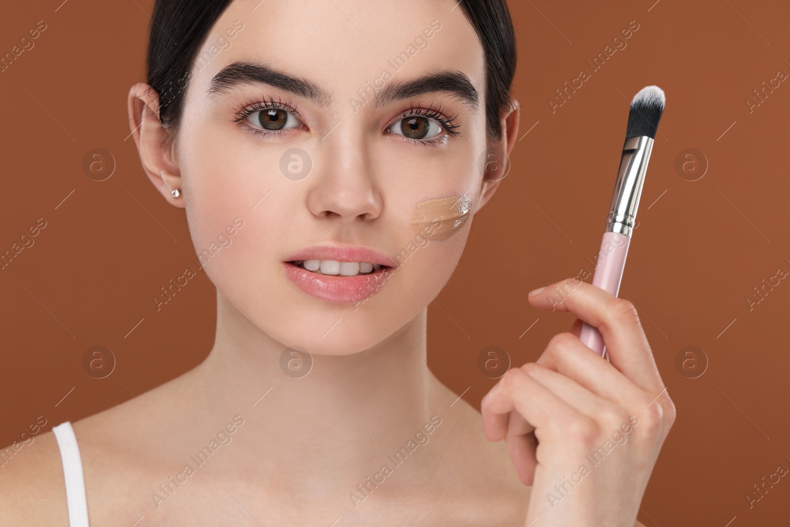 Photo of Teenage girl with swatch of foundation and makeup brush on brown background