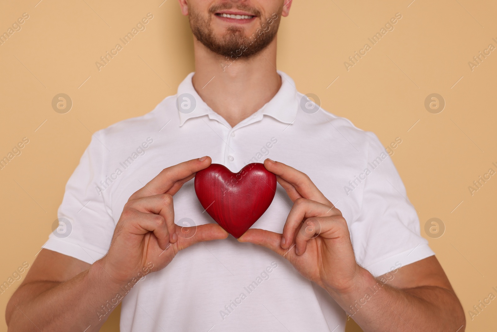 Photo of Happy volunteer holding red heart with hands on beige background, closeup