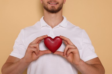 Photo of Happy volunteer holding red heart with hands on beige background, closeup