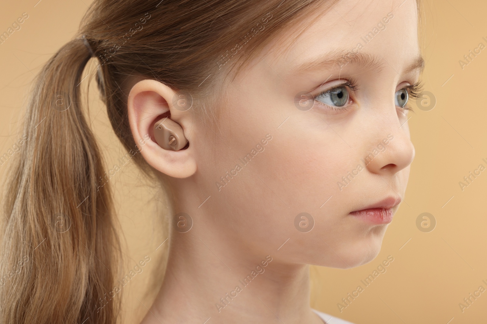 Photo of Little girl with hearing aid on pale brown background, closeup