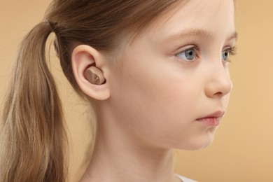 Little girl with hearing aid on pale brown background, closeup