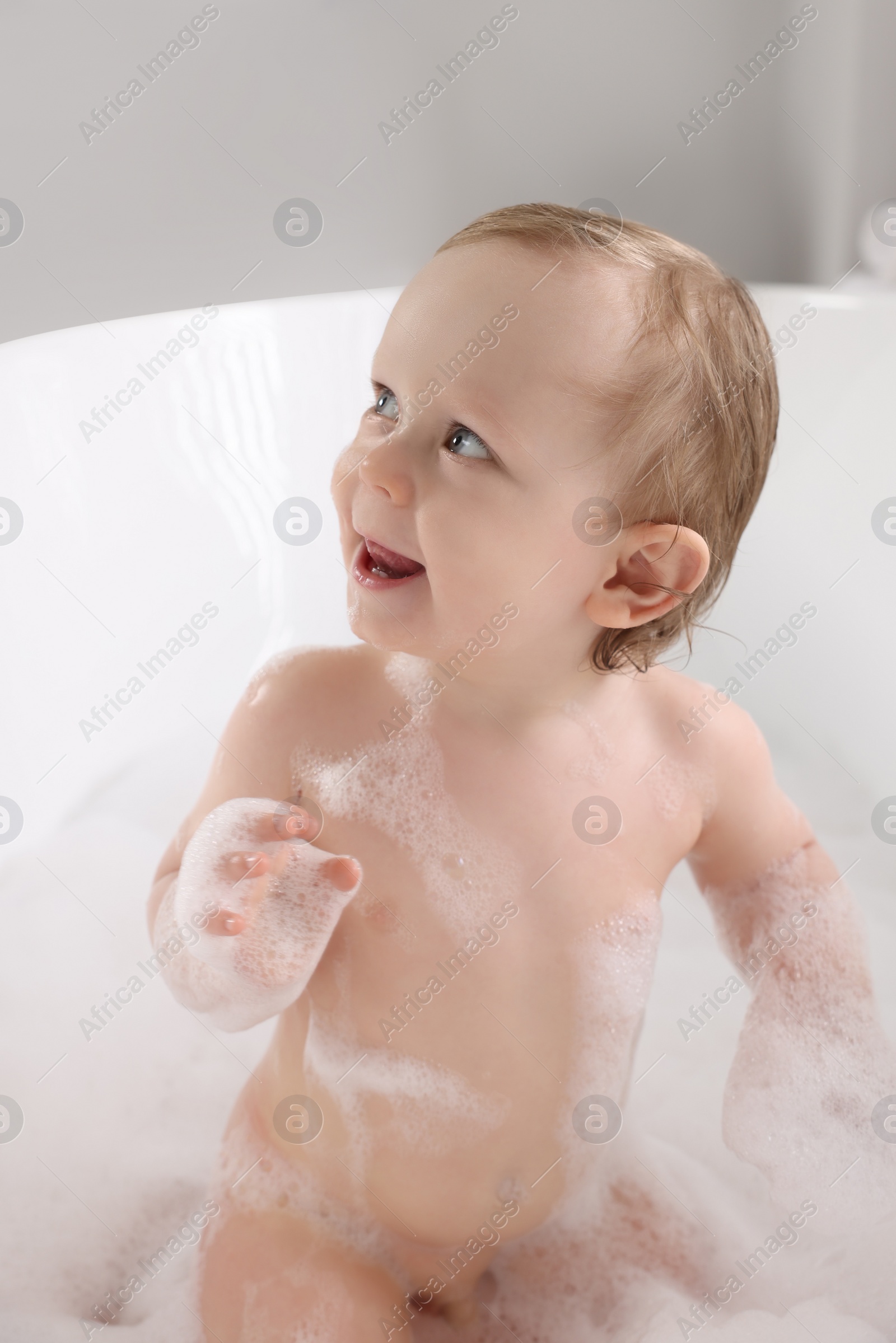 Photo of Cute little baby taking foamy bath at home