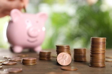 Many metal coins and piggy bank on wooden table against blurred green background. Space for text