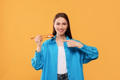 Photo of Happy beautiful young woman holding sushi with chopsticks on orange background
