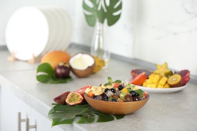 Delicious exotic fruit salad on light grey table in kitchen