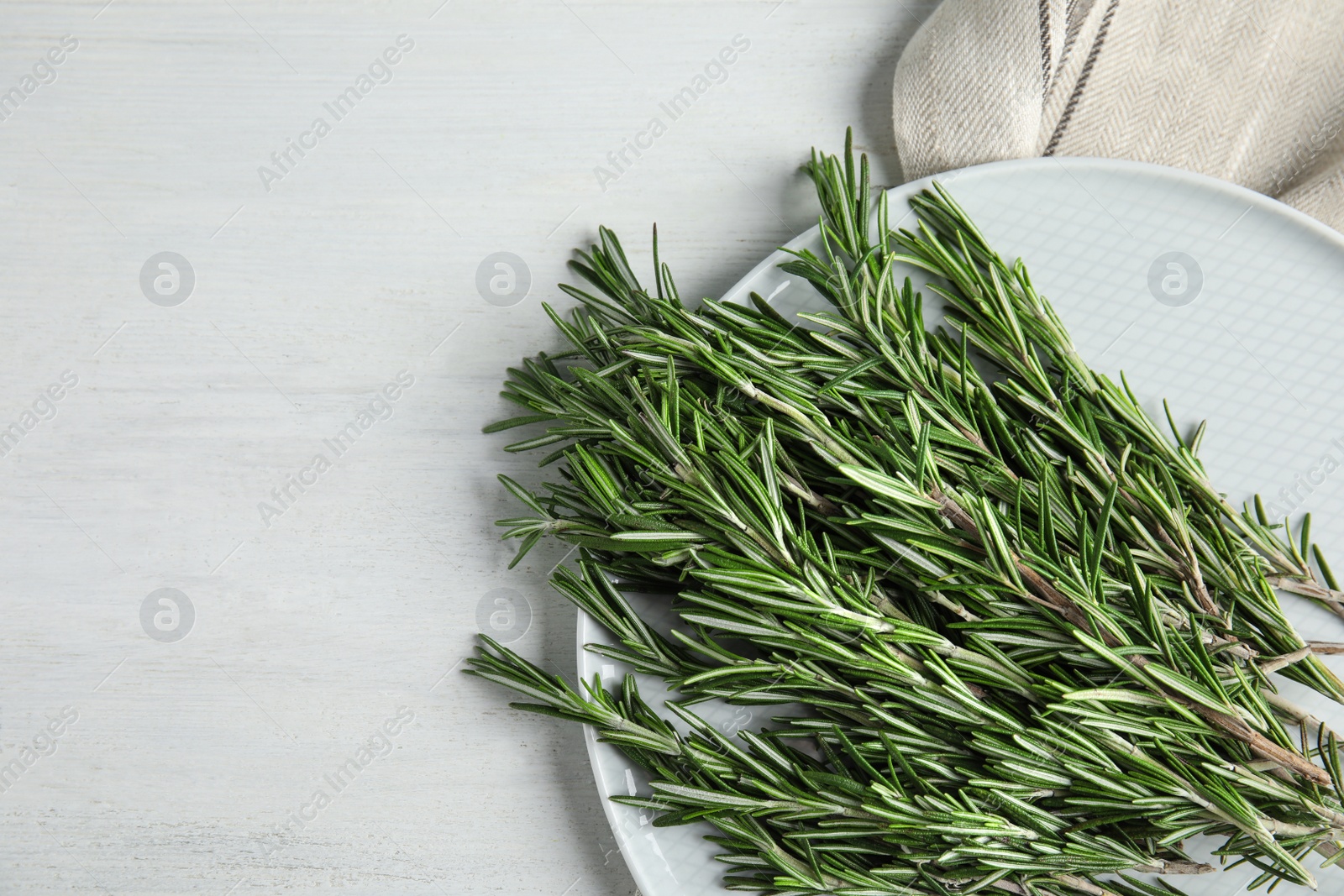 Photo of Plate with fresh rosemary twigs on wooden table, top view. Space for text