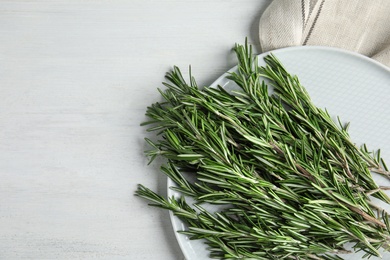 Photo of Plate with fresh rosemary twigs on wooden table, top view. Space for text