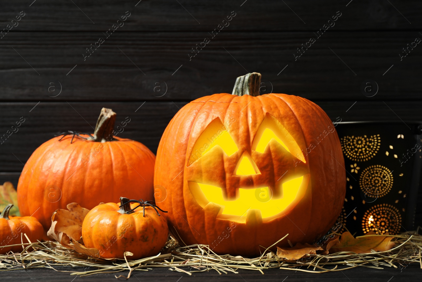 Photo of Jack o'lantern, pumpkins and straw on black wooden table. Halloween decor