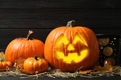 Photo of Jack o'lantern, pumpkins and straw on black wooden table. Halloween decor