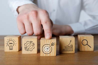 Image of Man touching cube with icon of target at wooden table, closeup