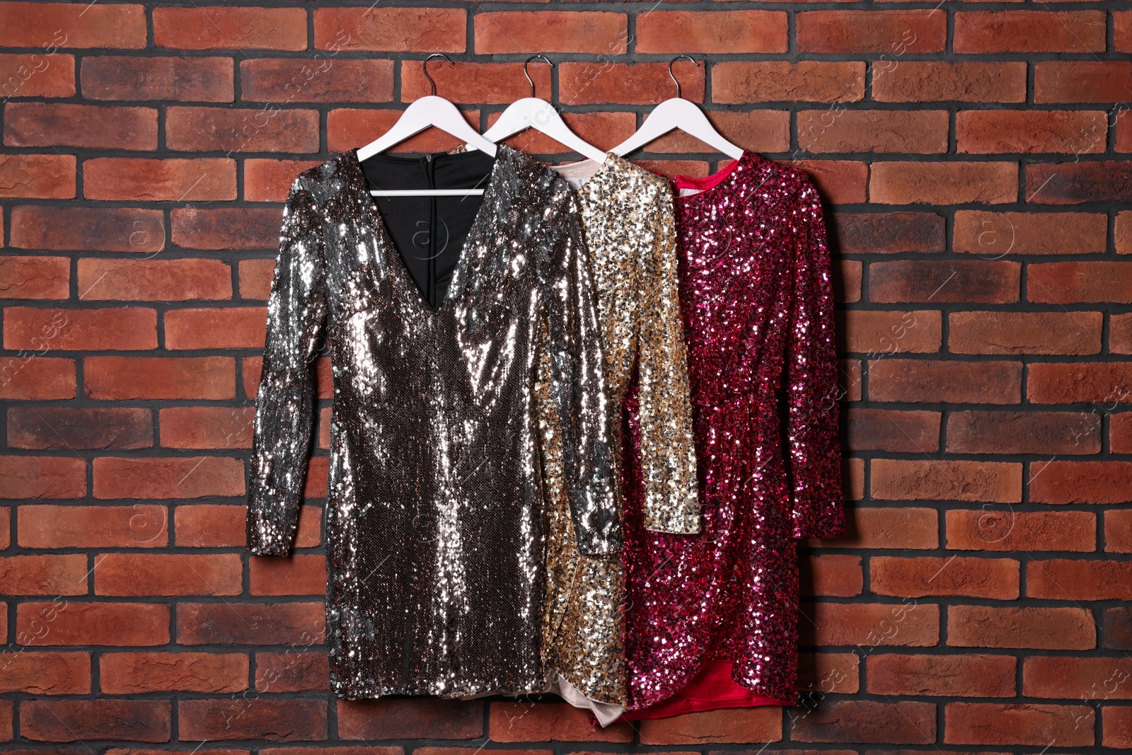 Photo of Different shiny beautiful women's party dresses on hangers near brick wall. Stylish trendy clothes for high school prom