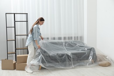 Photo of Young woman putting plastic film away from sofa at home