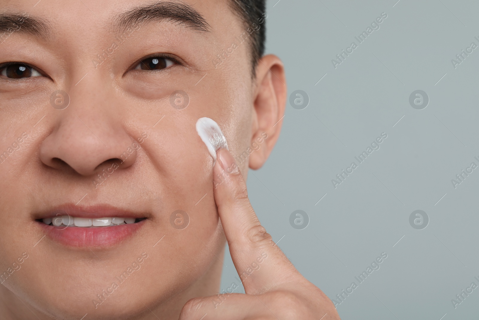 Photo of Handsome man applying cream onto his face on light grey background, closeup. Space for text
