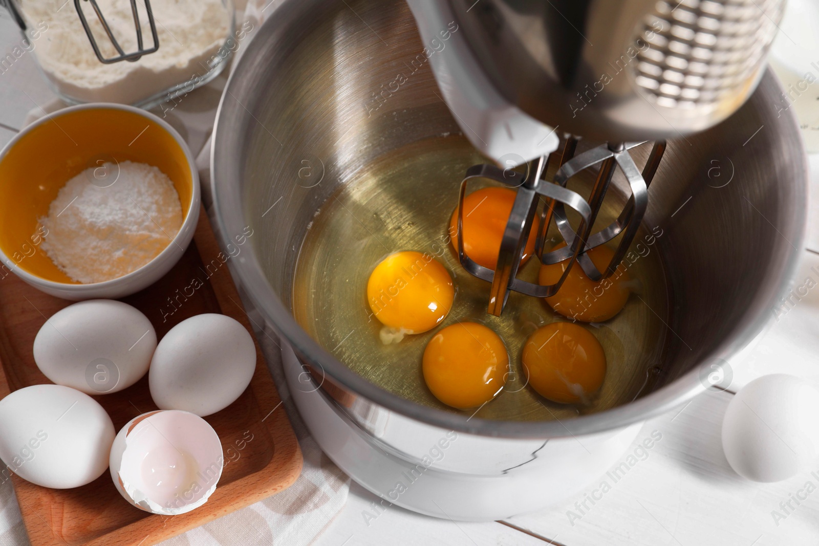 Photo of Making dough. Raw eggs in bowl of stand mixer on white table, closeup