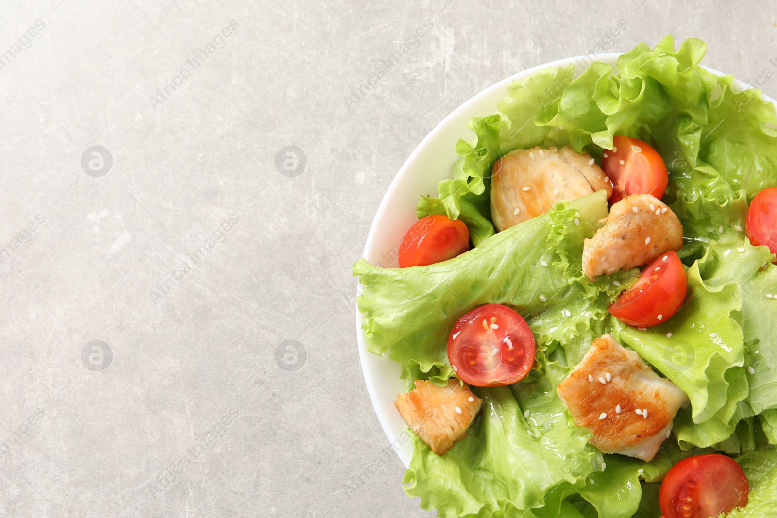 Photo of Delicious salad with chicken and cherry tomato on light grey table, top view. Space for text