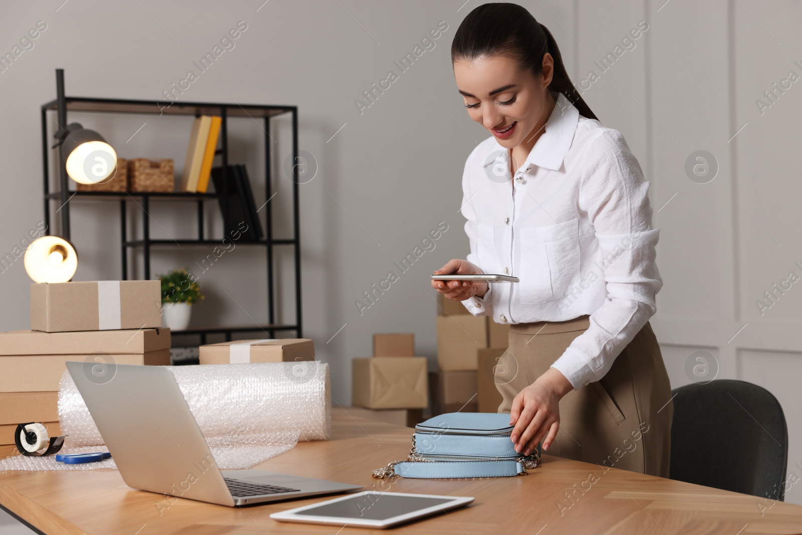 Photo of Seller taking picture of handbag at table in office. Online store